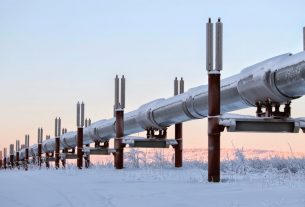 An energy supply pipe stretches across a snowscape, tinted by a pink sun, illustrating the impact of the conflict on gas and oil prices.