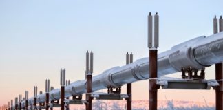 An energy supply pipe stretches across a snowscape, tinted by a pink sun, illustrating the impact of the conflict on gas and oil prices.
