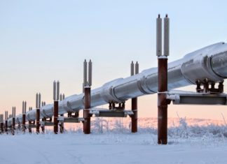 An energy supply pipe stretches across a snowscape, tinted by a pink sun, illustrating the impact of the conflict on gas and oil prices.