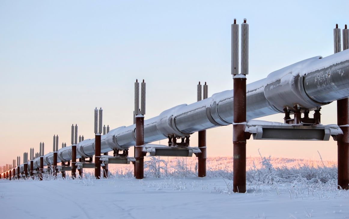 An energy supply pipe stretches across a snowscape, tinted by a pink sun, illustrating the impact of the conflict on gas and oil prices.